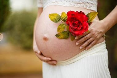 A photo of a pregnant woman holding her belly with a red rose in her hand