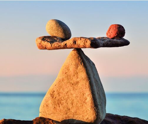 Three rocks balance on top of each other against a beautiful background of sky and water